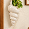 Cream ceramic shell-shaped wall planter styled with green foliage on a beige wall