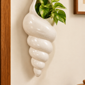 Cream ceramic shell-shaped wall planter styled with green foliage on a beige wall